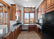 Thumbnail 32 of 64 - A community kitchen in the clubhouse at New Kent Apartments in West Chester, PA, featuring a large window, black appliances, a sink, and granite countertops