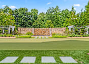 Thumbnail 57 of 59 - A green lawn with a brick wall and trees in the background.