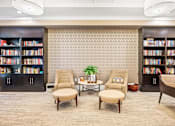 Thumbnail 23 of 59 - A room with a carpeted floor, two chairs, a table, and bookshelves filled with books.