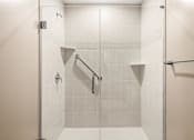 Thumbnail 8 of 59 - A white tiled shower with a glass door and a metal grab bar.