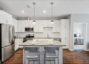 Thumbnail 3 of 39 - Modern luxury apartment kitchen featuring an oversized island, stainless steel appliances, gas range, quartz countertops, and light contemporary finishes at Claremont on the Square in Exton.