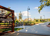Thumbnail 21 of 34 - A large green space with a walking trail, path lights, trees, bike station, and bridge near River Station apartment buildings.