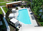 Thumbnail 13 of 34 - A sparkling resort-style pool near trees with lounge chairs, tables, chairs, and 3 shaded lounge areas.