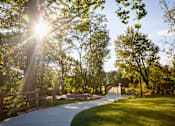 Thumbnail 22 of 34 - A beautiful trail with the sun shining through large trees and well-maintained grass leading to a bridge.