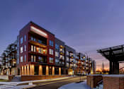 Thumbnail 25 of 34 - A corner street view of River Station's apartment buildings at sunset with trees and the capitol building in the background.