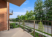 Thumbnail 18 of 39 - A balcony with a metal railing overlooks a street and greenery.