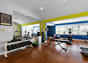 Thumbnail 26 of 30 - A state-of-the-art fitness center with free weights, weight lifting benches, cardio machines, hardwood-style flooring, recessed lighting, and large windows.