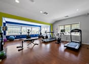 Thumbnail 25 of 30 - A spacious fitness center with beautiful hardwood flooring, large windows, cardio and weight equipment, a filtered water station, and large windows.