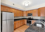 Thumbnail 4 of 30 - A U-shaped kitchen with stainless steel appliances, granite countertops, modern wooden cabinets, and hardwood-style flooring.