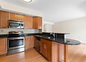 Thumbnail 5 of 30 - A kitchen with hardwood-style floors, black granite countertops, beautifully-designed breakfast bar, and stainless steel appliances.