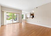 Thumbnail 6 of 30 - A spacious living room with hardwood style flooring and large sliding glass doors to a private patio near a dining area and kitchen.