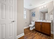 Thumbnail 23 of 30 - A white door is on the left of a bathroom with a toilet, sink and mirror.