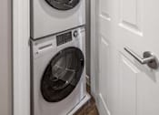 Thumbnail 20 of 30 - A white door is open to reveal a white washer and dryer stacked on top of each other.
