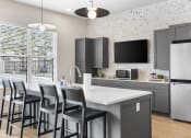 Thumbnail 7 of 28 - a kitchen with gray cabinets and a white island with chairs at The Junction at Rogers, Rogers, Arkansas