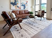 Thumbnail 18 of 28 - A living room with a brown leather couch, a brown chair, and a patterned rug.