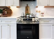 Thumbnail 10 of 28 - A modern kitchen with white cabinets and a stainless steel oven.