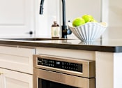 Thumbnail 12 of 28 - A modern kitchen with a stainless steel oven and a bowl of green apples on the counter.