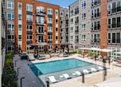 Thumbnail 14 of 46 - A swimming pool surrounded by lounge chairs and umbrellas in front of apartment buildings.