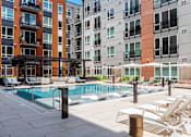 Thumbnail 15 of 46 - A pool area with sun loungers and a building in the background.