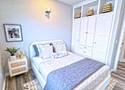 Thumbnail 7 of 18 - A bedroom with a bed, a ceiling fan, and a cabinet with baskets on top.