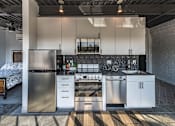 Thumbnail 28 of 39 - Steelcote Crossing kitchen with white cabinetry, black quartz countertops, stainless steel appliances, black tile backsplash and concrete floors at Steelcote Square, Missouri, 63103