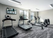 Thumbnail 16 of 28 - a gym with various cardio machines and a tv on the wall at Hibernia Apartments, St Louis, MO, 63139