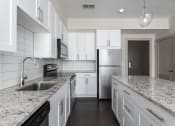 Thumbnail 2 of 28 - Hibernia kitchen with white cabinets, white tile backsplash, granite countertops and stainless steel appliances at Hibernia Apartments, St Louis, MO
