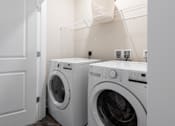 Thumbnail 11 of 28 - Two white front load washing machines in a laundry room at Hawk Ridge Apartments, Lake St. Louis, MO 63367