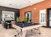 Thumbnail 18 of 28 - A pool table is in the middle of a room with a brown floor and orange walls at Montage at Hawk Ridge Apartments, Lake St. Louis, 63367, Missouri