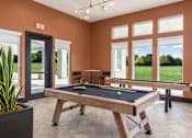 Thumbnail 19 of 28 - A pool table in a room with orange walls and a view of a green lawn outside the window at Montage at Hawk Ridge Apartments, 63367, MO