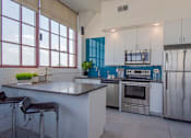 Thumbnail 35 of 39 - Steelcote Lofts kitchen with Steelcote blue backsplash, gray quartz countertops, stainless steel appliances, white cabinetry, kitchen island and polished concrete floors at Steelcote Square, St. Louis