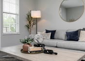 Thumbnail 10 of 36 - A living room with a grey couch, a wooden coffee table, and a round mirror on the wall. at The Cunningham Apartments, Apartments, West Des Moines, IA