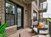 Thumbnail 17 of 36 - A patio with a couch and a chair is on a brick building. at The Cunningham Apartments, West Des Moines, Iowa