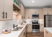 Thumbnail 52 of 71 - a modern kitchen with white counter tops and wooden cabinets at The Flats & Terraces at Wildhorse Village, Chesterfield, 63005