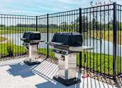 Thumbnail 29 of 34 - Two barbecue grills are placed on a patio with a view of a lake.