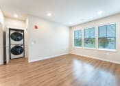 Thumbnail 4 of 18 - living room with open floorplan and modern kitchen with white cabinets, stainless steel appliances, plank vinyl flooring and stackable washer and dryer at Pure Lowell, Arkansas