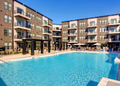 Thumbnail 29 of 36 - A large swimming pool is surrounded by apartment buildings. at The Cunningham Apartments, West Des Moines, IA, 50266