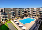 Thumbnail 28 of 36 - A large swimming pool is surrounded by sun loungers in front of apartment buildings. at The Cunningham Apartments, Apartments, West Des Moines, IA