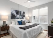 Thumbnail 15 of 71 - main bedroom with rich plank flooring, oversized windows with custom shades, ceiling fan, large bed, nightstands and accent table at The Flats & Terraces at Wildhorse Village, Chesterfield Missouri