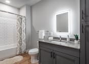 Thumbnail 13 of 18 - A modern bathroom with a white toilet, a sink with a mirror, and a shower with a glass door.
