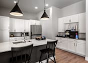 Thumbnail 17 of 18 - A modern kitchen with a white countertop and black chairs.
