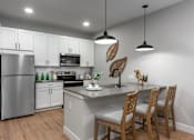 Thumbnail 18 of 18 - A kitchen with a refrigerator, microwave, oven, sink, and wooden chairs.