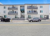 Thumbnail 2 of 13 - A car is parked on the side of a street in front of a building.