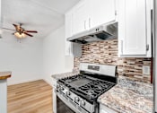 Thumbnail 4 of 12 - A kitchen with a stove and a fan on the ceiling.