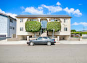 Thumbnail 1 of 5 - A car is parked in front of a two-story building with green plants on the front.