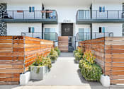 Thumbnail 10 of 31 - A modern building with a black door and windows, surrounded by wooden fences and plants.