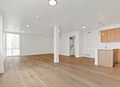 Thumbnail 1 of 12 - A spacious room with wooden flooring and white walls.