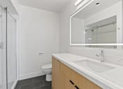 Thumbnail 6 of 12 - A white bathroom with a toilet, sink, and mirror.
