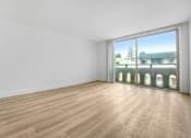 Thumbnail 12 of 56 - A room with wooden flooring and a large window overlooking a building.