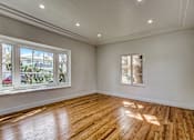 Thumbnail 1 of 16 - A room with wooden floors and white walls, with windows showing an outdoor view.